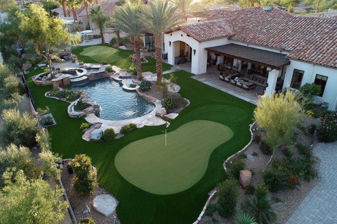 Luxurious backyard with a golf green, pool, and palm trees in a sunny landscape.