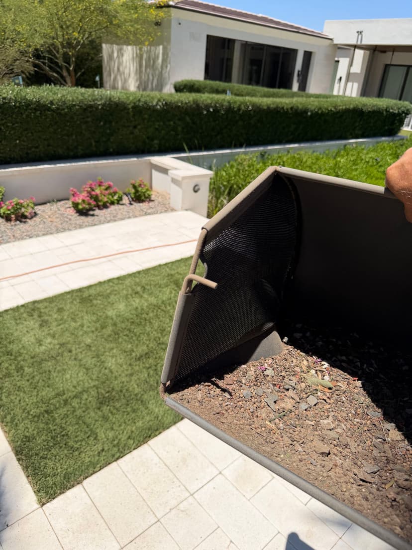 Person holding a container with soil, near a well-maintained garden and green lawn.